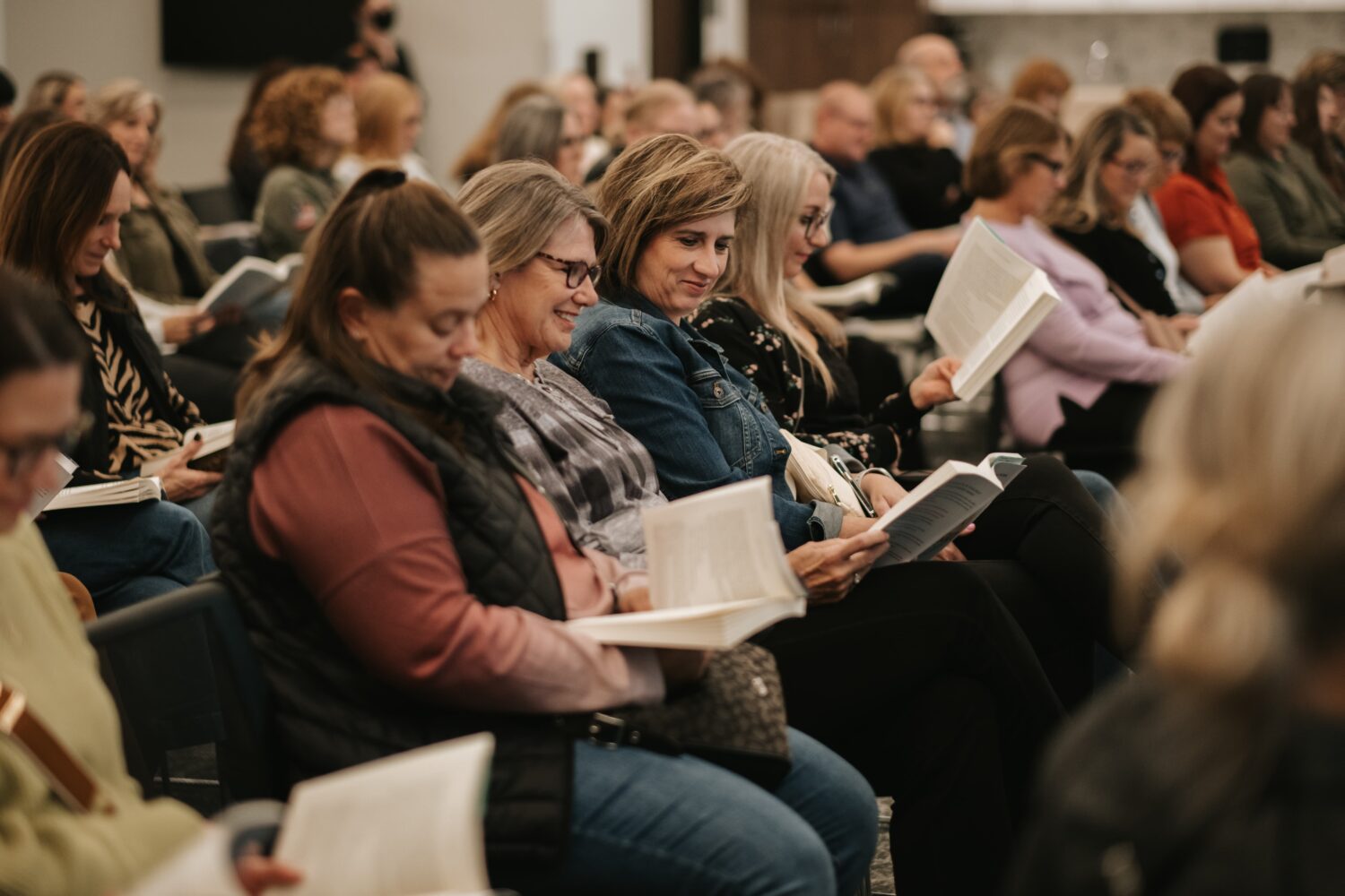 women sit in a row as they flip through open books on their laps