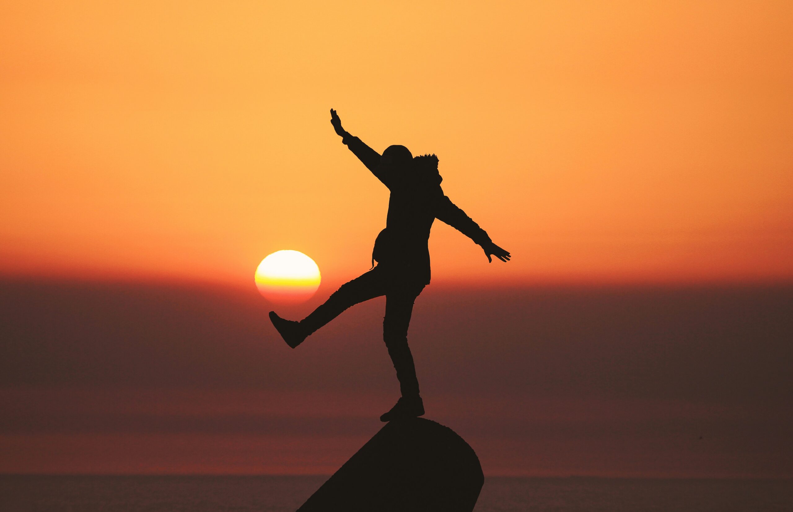 Person climbing on rock with sunset in background