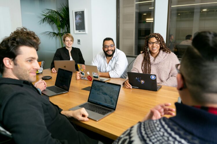 A group of people seated at a conference room table with laptop computers.