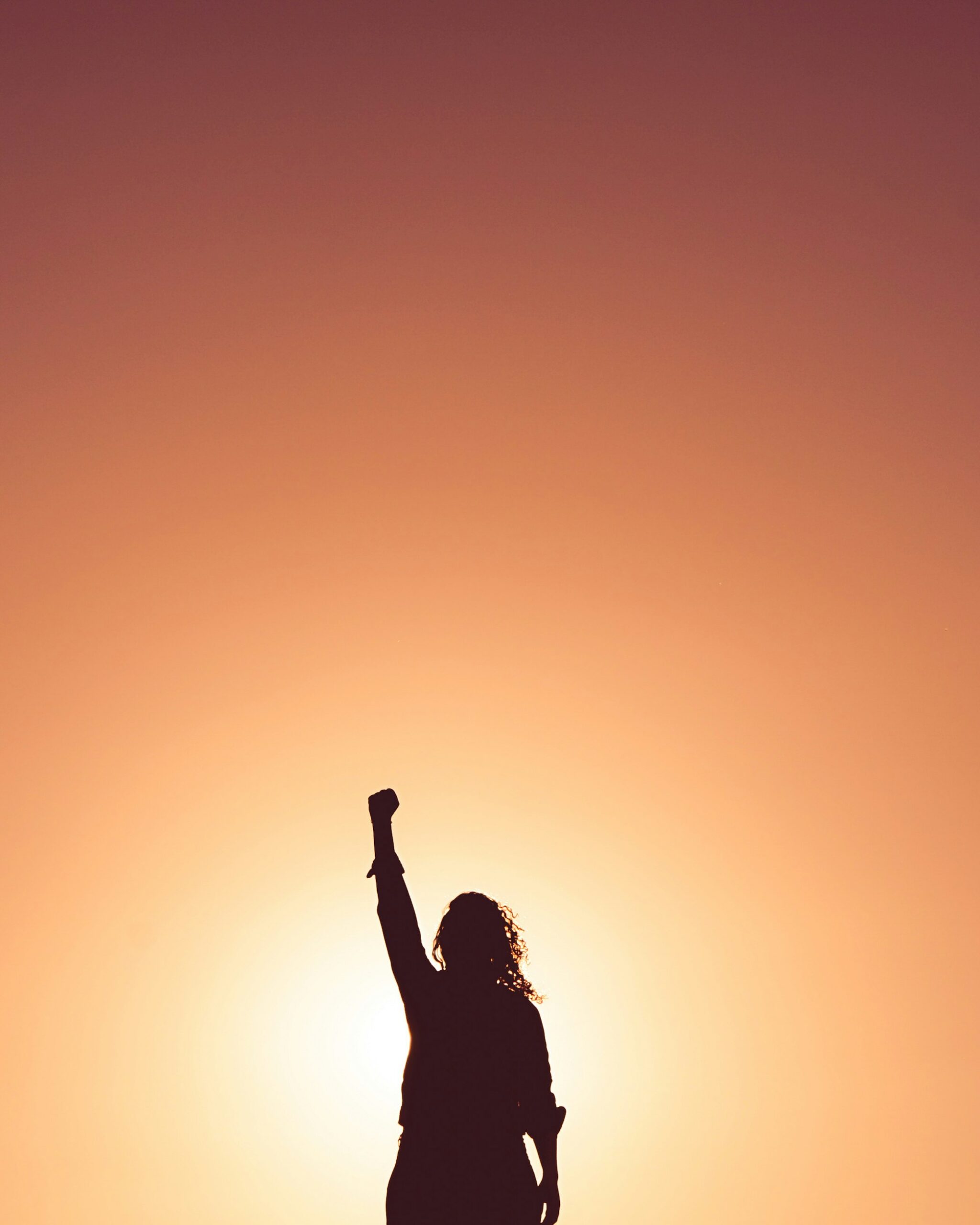 Woman stands with her arm raised in a fist as she is backlit by the setting sun