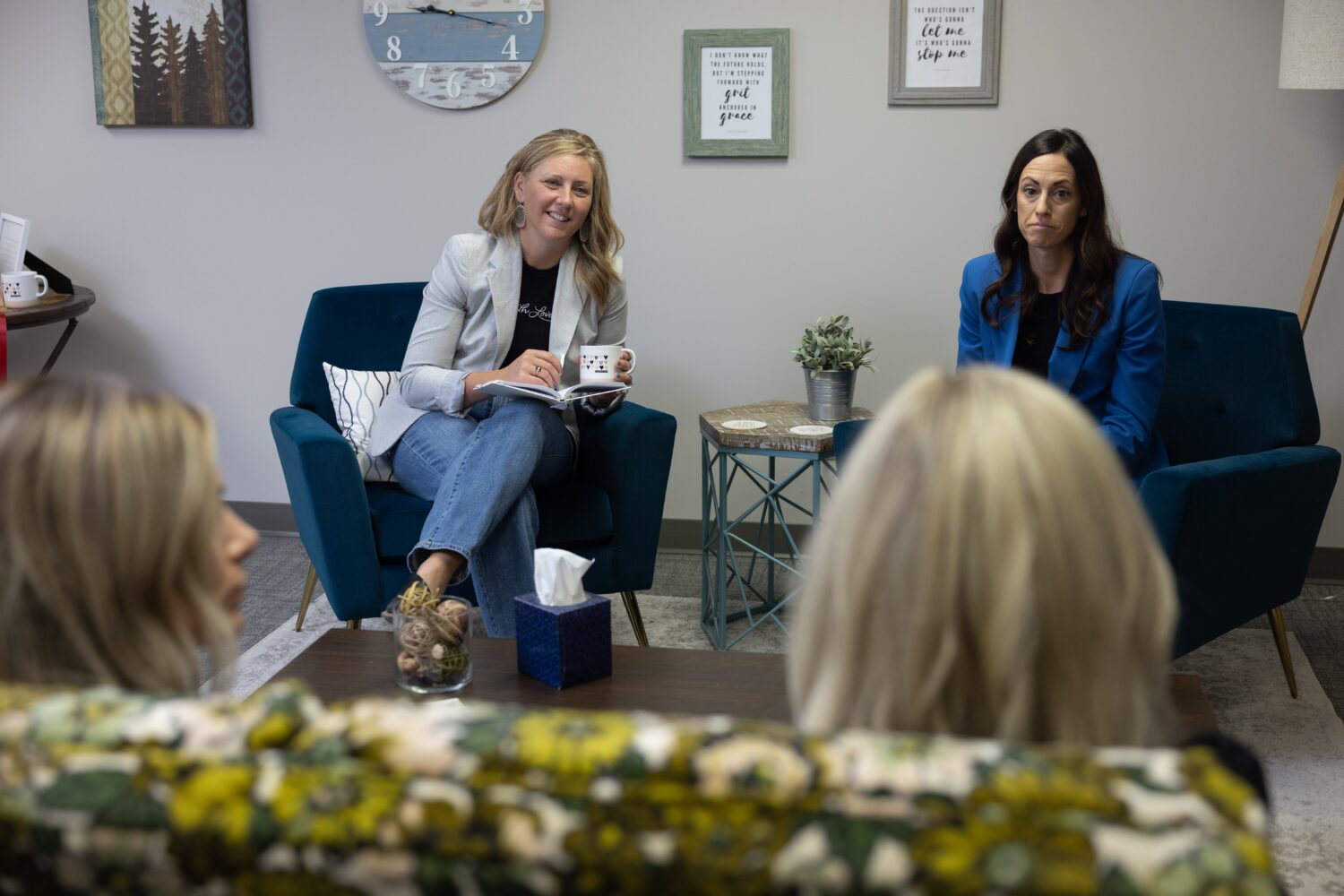 Two women engage in a group discussion in a cozy setting with couches and chairs