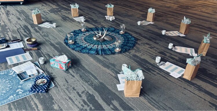 A mandala is set up in a carpeted space, surrounded by gift bags and papers.
